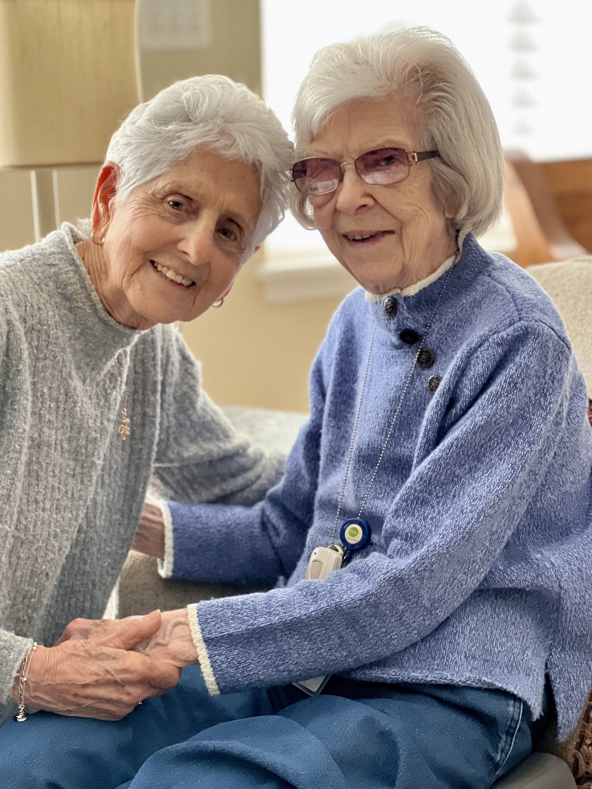 Two elderly women holding hands and looking at the camera.