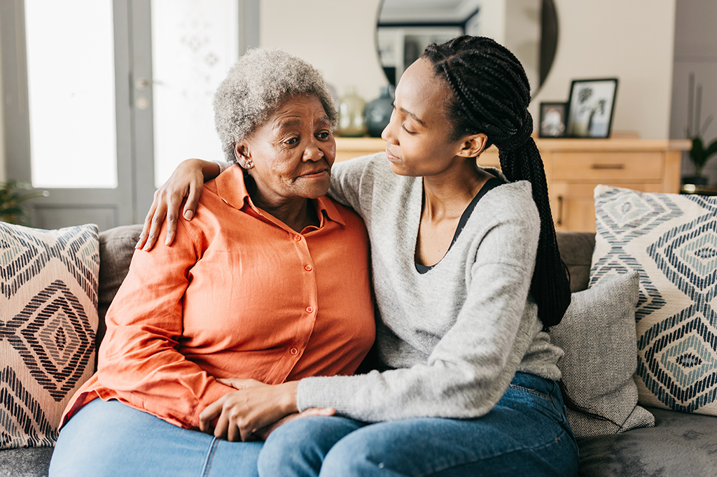 Young woman comforting mother on sofa at home Photo of young woman comforting mother on sofa at home